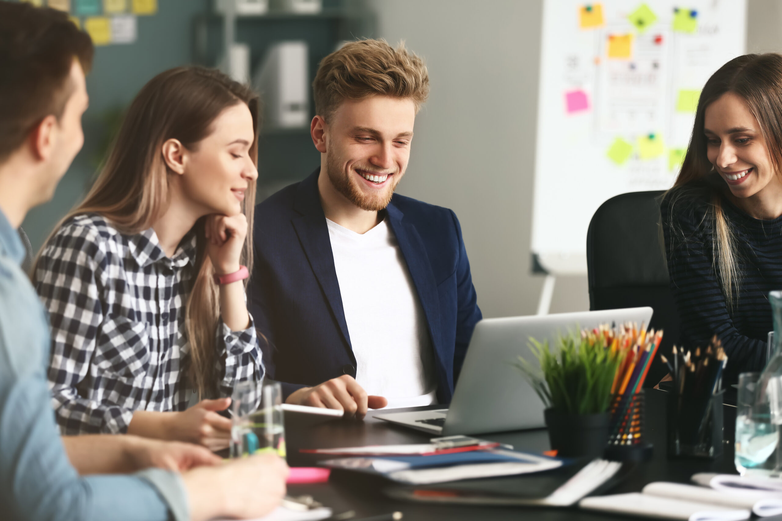 Young IT specialists working in modern office Two men and two women IT specialist smiling while looking at a laptop screen on a desk