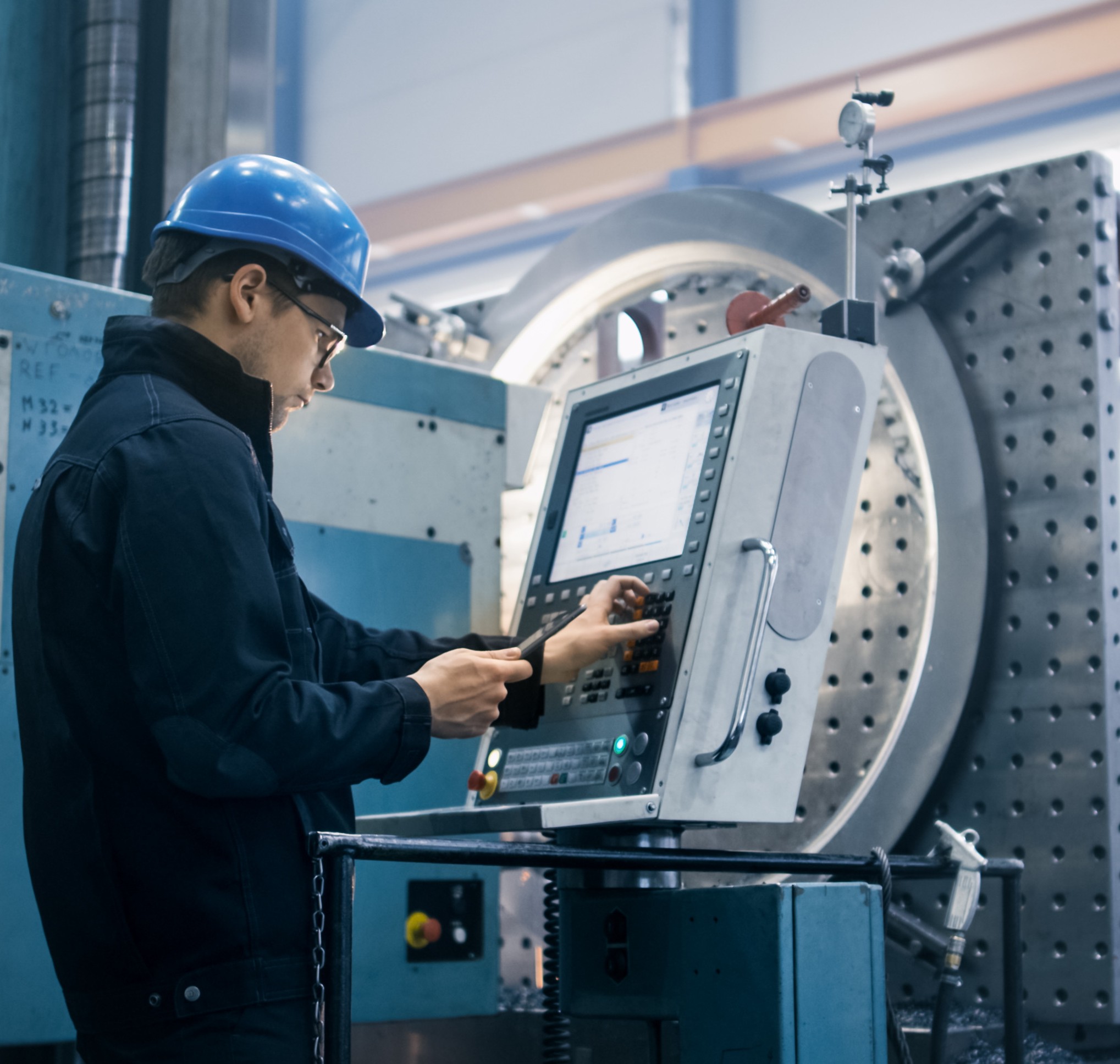 Factory worker is programming a CNC milling machine with a tablet computer. Engineer programming on a touchscreen in a warehouse